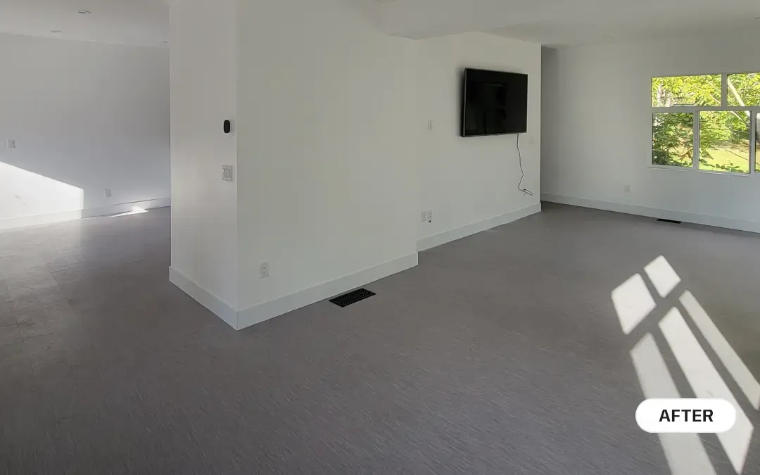 An after photo of a bright, newly renovated living space featuring light grey flooring, smooth white walls, new baseboards, and a wall-mounted television by PCC Renovations.